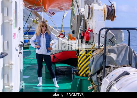 Eine Frau steht selbstbewusst auf dem Deck eines Forschungsschiffes in Russland, in lässiger Kleidung gekleidet. Helles Sonnenlicht beleuchtet ihre Umgebung als das o Stockfoto