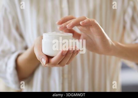 Nahaufnahme der weiblichen Hände, die einen weißen Behälter mit Körpercreme halten Stockfoto