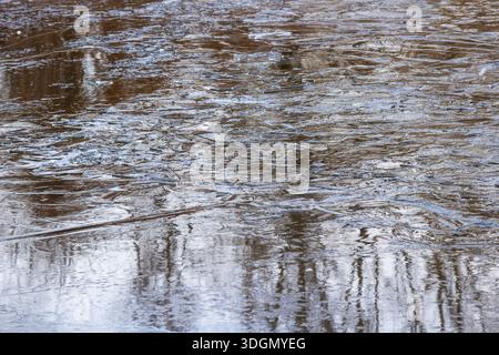 Dünnes Eis auf einem Fluss und Bäume spiegeln sich im Wasser. Winterhintergrund Stockfoto