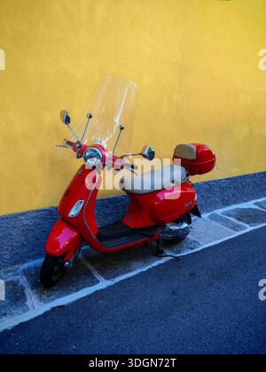 Roter italienischer Roller parkte in der Nähe des Hauses mit gelber Mauer an der Straße Stockfoto