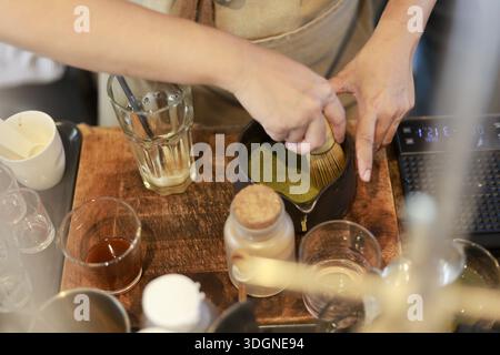 Nahaufnahme professioneller Barista, der mit der Hand sorgfältig organisches Matcha-Grüntee-Pulver in einer Schüssel auf einer Holztheke mit konzentrierter Zubereitung rührt Stockfoto