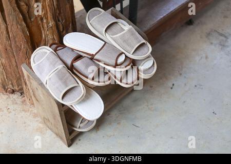 Hausschuhe aus Naturstoff, die auf einem Holzschuhregal vor dem Zimmer platziert werden, sorgen für eine angenehme, entspannende Stimmung am Urlaubswochenende mit weichen Schuhen Stockfoto