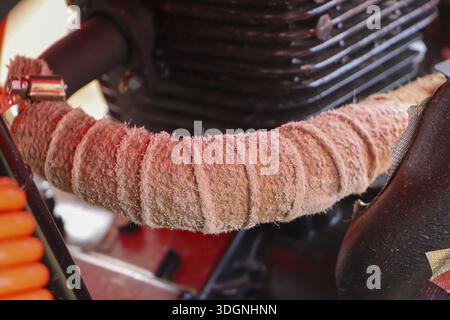 Nahaufnahme des Auspuffrohrs eines kundenspezifischen Motorrads, das mit beigefarbenem wärmeisolierendem Tuch in der Nähe des Motors gewickelt ist, zeigt mechanische Textur und robusten Stil für Stockfoto
