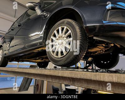 Nahaufnahme der Tiefwinkelansicht einer Fahrzeuginspektion an einem Servicelift in einer Garage. Das Reifenmuster wurde geändert, sodass es nicht mehr erkennbar ist. Stockfoto