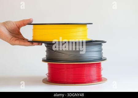 Gelbe, graue und rote Kunststofffilamente für den 3D-Druck auf Spulen und einer Frauenhand auf weißem Hintergrund, 3D-Druckermaterial, Rohstoffe für Männer Stockfoto