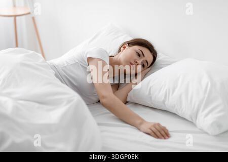 Deprimiert traurige, unglückliche europäische tausendjährige Frau, die allein zu Hause auf weißem Bett liegt und traurig über ihren Mann ist Stockfoto