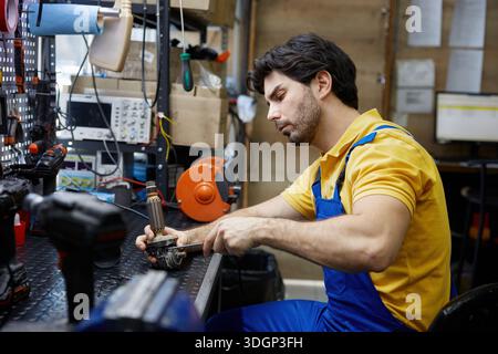 Techniker, Servicemitarbeiter, der eine defekte Bohrmaschine in einer viel beschäftigten Werkstatt repariert Stockfoto