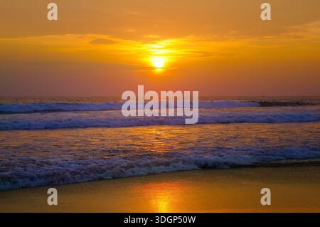 Wunderschöner Sonnenuntergang über Meer oder Meer. Lebendige und weiche Farben, magisches Licht. Kleine Wolken am Himmel, Spiegelung der Sonne im Wasser und Sand am Strand. Stockfoto