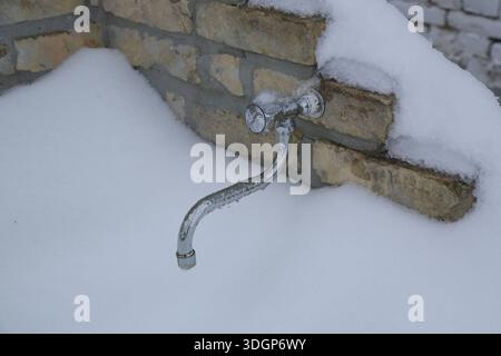 Wasserhahn aus Metall im Freien, der im Winter bei kalter Temperatur von Schnee bedeckt ist Stockfoto