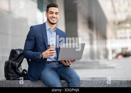 Positiver Typ aus dem Nahen Osten mit Laptop, der eine Kaffeepause im Freien hat Stockfoto