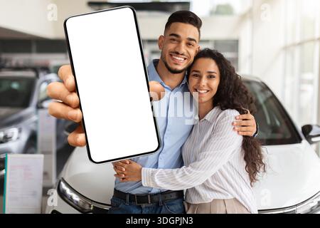 Liebevolle muslimische Familie zeigt Smartphone mit leerem Bildschirm, kauft Auto Stockfoto