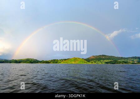 Ein lebhafter Regenbogen überzieht den Mutanda-See in Kisoro im Südwesten Ugandas, während das Sonnenlicht durch vorbeiziehende Regenwolken bricht und sich auf dem ruhigen Berg reflektiert Stockfoto