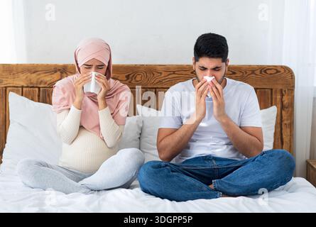 Muslimische Schwangere bekam Grippe, hatte laufende Nase, saß auf dem Bett und bläste die Nase, niest im Papiertaschentuch Stockfoto