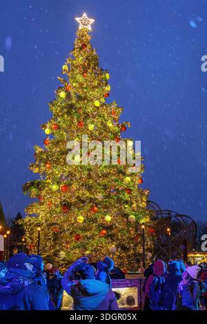 Die Menschen versammeln sich am großen Weihnachtsbaum, der das Distillery District bei Nacht schmückt, wenn der Schnee fällt. Stockfoto