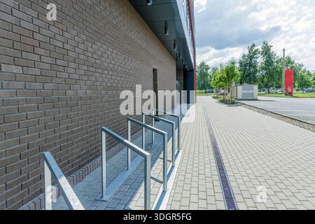 Seitenansicht eines modernen Bürogebäudes mit dunklen Ziegelwänden, Fahrradständern aus Metall und einem sauberen Steingang an einem sonnigen Tag. Stockfoto