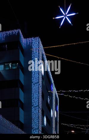Städtische Büroarchitektur, beleuchtet mit festlichen blauen LED-Lichtern und einem aufgehängten Neonstern in einer dunklen Winternacht in Barcelona. Stockfoto