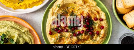 Ein lebhaftes Angebot zeigt verschiedene Arten von Hummus, darunter Klassik, Rote Bete, Brokkoli und Kurkuma. Begleitet von Oliven und Brotstäbchen, ist es drin Stockfoto