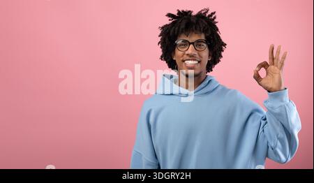 Porträt eines glücklichen afroamerikanischen Teenagers, der eine OK-Geste auf einem rosa Studiohintergrund zeigt, Panorama mit leerem Raum Stockfoto