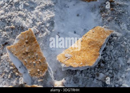 Gelbe Farbstücke auf vereistem Untergrund verstreut, Nahaufnahme der beschädigten Straßenoberfläche bei kalten Winterbedingungen Stockfoto