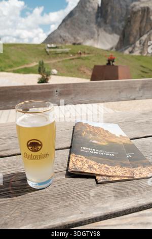 Tisch mit kaltem Glas Bier und Hüttenmenü auf der Terrasse der italienischen Hütte Tierser Alp in Südtirol. Stockfoto