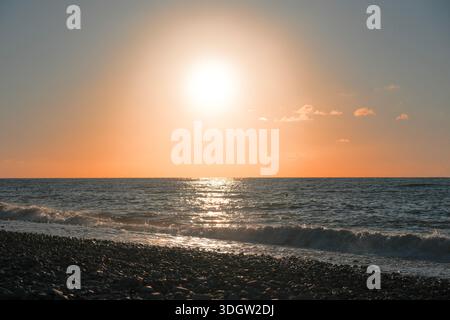 Sonnenuntergang über dem Schwarzen Meer in Batumi, Georgia, mit sanften Wellen und warmem orangefarbenem Licht, das sich am Horizont reflektiert. Stockfoto