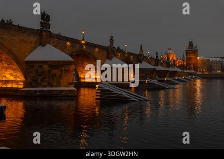 Die Karlsbrücke leuchtet mit künstlichem Licht, das am dunklen Winterabend in Prag auf der Moldau reflektiert Stockfoto