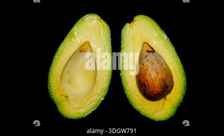 Zwei Hälften frischer reifer Avocado mit Samen, die cremige Textur auf dunklem, stimmungsvollem Hintergrund zeigen. Stockfoto