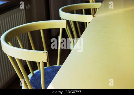 Leere gelbe Stühle neben dem Tisch in der sonnendurchfluteten Küche mit großer Tischplatte, die Platz zum Kopieren bietet. Stockfoto