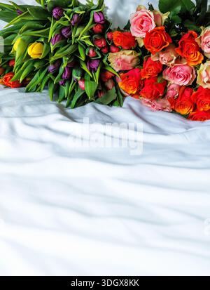 Gemischte Sträuße aus Rosen und Tulpen liegen in einem Schlafzimmer auf einer Bettdecke. Großer Kopierbereich Stockfoto