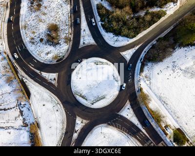 Fahrzeuge, die im Kreisverkehr mit geklärtem schwarzem Asphalt in weißem Schnee fahren Stockfoto