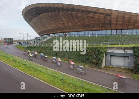 Straßenradfahrer, die auf einer Outdoor-Fahrradstrecke mit dem Lee Valley Velodrome im Hintergrund rasen, sind verschwommen. Queen Elizabeth Olympic Park, Stratford, E20. Stockfoto