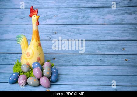 Buntes Hühnchen mit Ostereiern auf einem Korb auf hölzernem Hintergrund mit Kopierraum Stockfoto