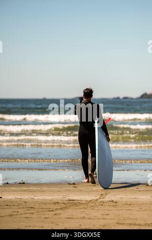 Ein Mann in einem Neoprenanzug, der im Wasser spaziert und bereit ist, in Tofino Kanada einige killernde Meereswellen zu surfen Stockfoto