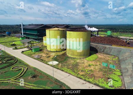 Ein hochwinkliger Drohnenschuss, der zwei riesige gelbe und grüne Lagertanks für Rohpalmöl in einer modernen Verarbeitungsanlage innerhalb einer großen Plantage erfasst Stockfoto
