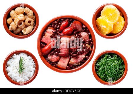 Traditionelle brasilianische Feijoada isoliert auf weißem Hintergrund, begleitet von weißem Reis, geschnittenem ​​kale, Orange und Schweinefleisch in Tonschalen. Oben Stockfoto