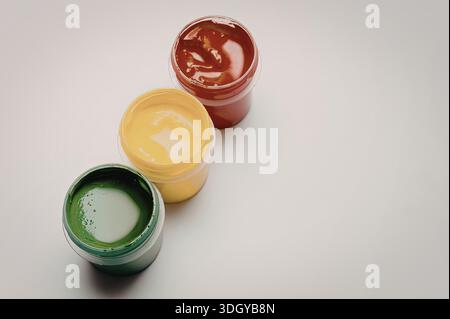 Ein Bild mit drei offenen Farbgläsern in den Primärfarben Rot, Gelb und Grün. Jedes Gefäß wird nebeneinander platziert, um die lebendigen Farben freizugeben Stockfoto