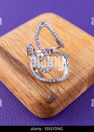 Nahaufnahme eines silbernen Rings mit geschwungenen Linien und weißen Strasssteinen auf hölzernem Hintergrund. Stockfoto