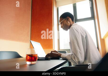 Ein junger Erwachsener konzentriert sich auf sein Notebook in einem lebendigen, modernen Bürobereich. Stockfoto