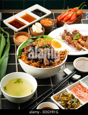 Köstliches asiatisches Nudelgericht mit verschiedenen Gewürzen und Beilagen auf einem wunderschön gedeckten Tisch. Stockfoto