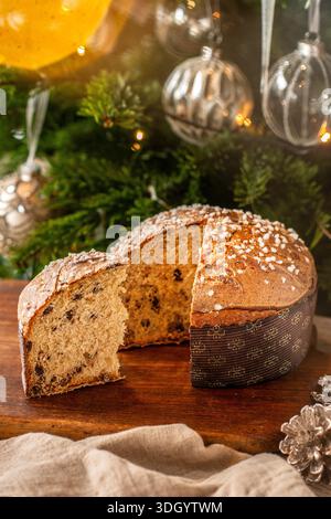 Ein köstliches Stück traditioneller italienischer Panettone mit Schokoladenchips, neben dem ganzen Kuchen mit einem geschmückten Weihnachtstrie Stockfoto