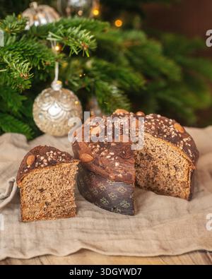 Ein Stück traditioneller Panettone mit Mandeln und Perlzucker vor einem geschmückten Weihnachtsbaum. Stockfoto