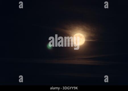 Ein heller Vollmond scheint durch dünne Wolken in einem dunklen Nachthimmel. Dezenter atmosphärischer Nebel und sanftes Licht schaffen eine ruhige, geheimnisvolle Stimmung mit Stockfoto