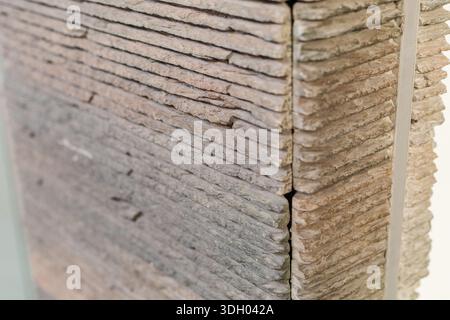 Zementplatten mit einer strukturierten Oberfläche werden zusammen platziert und zeigen ihre unterschiedlichen Schichten. Die Einstellung ist in Innenräumen, wahrscheinlich bei einer Designveranstaltung oder Stockfoto