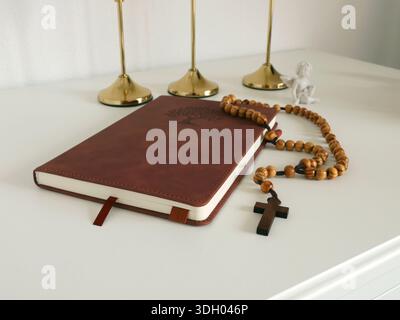 Katholische Ecke zu Hause. Hölzerne Rosenkranzperlen, Kreuz und Gebetsbuch. Glaube, Symbole und Traditionen. Stockfoto