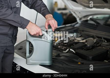 Unbekannter Mann, der Motorölbehälter in der Nähe des Motormotors öffnet, sich auf den Ölwechsel oder die Fahrzeugwartung in der Automobilwerkstatt vorbereitet, Hände und Arme in Nahaufnahme sichtbar Stockfoto