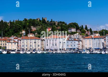 Uferpromenade mit Reihen von Segelbooten im Hafen und den historischen Stadtmauern auf dem üppigen Hügel in der Ferne. Stockfoto
