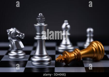 Silbernes Königschachstück, das siegreich über gefallenes goldenes Königschachteil auf Schachbrett steht. Konzept von Strategie, Sieg und Führung. Stockfoto