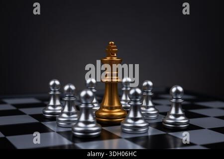 Goldener Schachkönig umgeben von silbernen Schachfiguren auf Schachbrett. Stockfoto