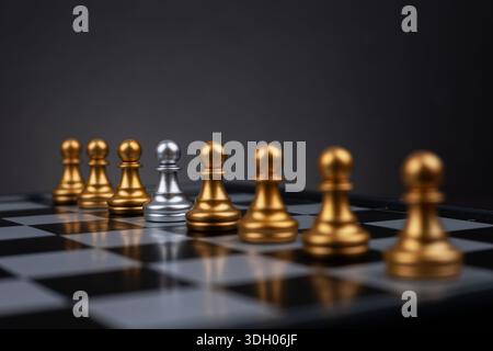 In der Mitte einer Reihe goldener Bauern steht ein silberner Bauern, der entweder die unterschiedlichen Merkmale der Akzeptanz der Gruppe anmerkt. Stockfoto