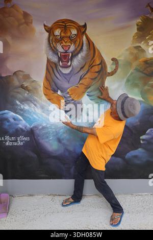 Ein talentierter thailändischer Tempelkünstler posiert vor seinem herrlichen Wandbild eines Tigerangriffs und sieht, wie es zum Leben erweckt Stockfoto